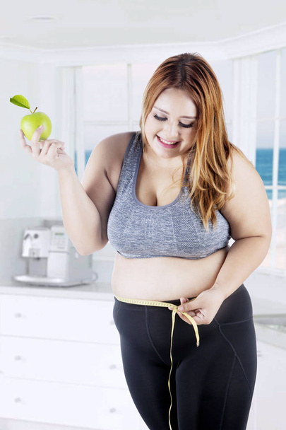 Overweight woman measures her belly in kitchen - Foto, Bild