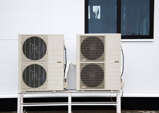 Δύο εξωτερικές μονάδες κλιματιστικών μηχανημάτων στέκεται στο έδαφος μπροστά από την πρόσοψη του σύγχρονου κτιρίου - Φωτογραφία, εικόνα