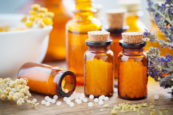 Bottles of homeopathic globules, mortar, healing herbs and flowers. - 写真・画像