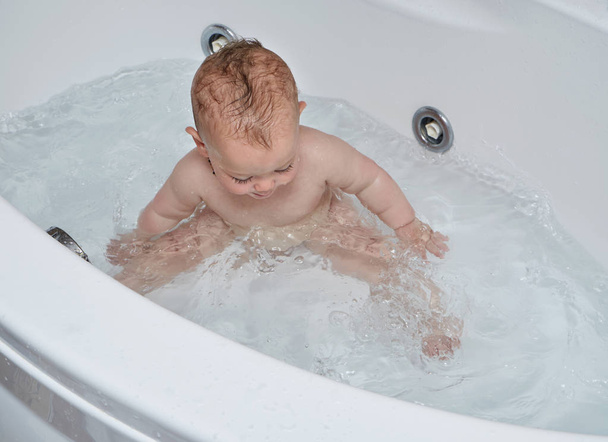 Portrait of an infant male playing with water in a bath tub - Foto, afbeelding