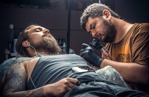 Tatuaje profesional haciendo un tatuaje en el salón de tatuajes. / Tatuaje profesional en el trabajo en el salón de tatuajes
. - Foto, Imagen