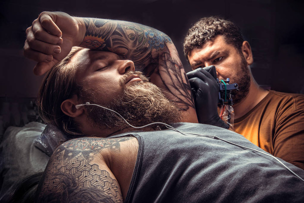 Profesjonalnych tattooist co tatuaż tattoo studio. / profesjonalne tattooer sprawia, że tatuaż zdjęcia w tatuażu. - Zdjęcie, obraz