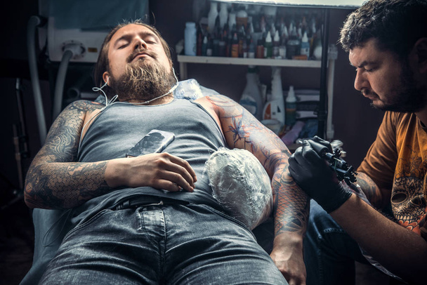 Tattooist profesjonalne pozowanie w tattoo parlor. / profesjonalne tattooer sprawia, że tatuaż zdjęcia w studio tatuażu. - Zdjęcie, obraz