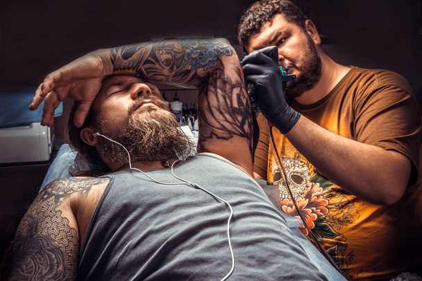 Maestro haciendo tatuaje en estudio de tatuaje. / Tatuaje especialista posando en salón de tatuaje
. - Foto, Imagen