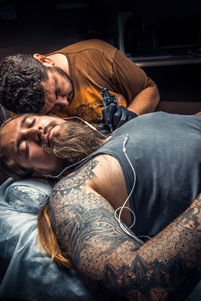 Master works in studio./Professional tattooist working tattooing in tattoo parlour. - Photo, Image