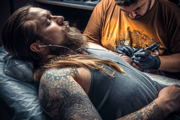 Татуировщик создает татуировку в студии. / Профессиональный татуировщик работает татуировщиком в салоне
. - Фото, изображение