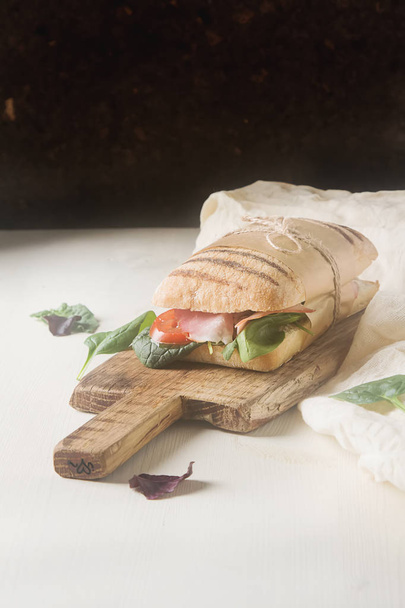 French baguette with sausage, tomatoes and lettuce. Light backgr - Photo, image