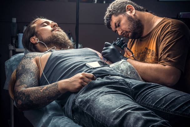 Tatuaje profesional en el trabajo en el estudio de tatuajes. / Especialista en tatuajes posando en el salón de tatuajes
. - Foto, Imagen