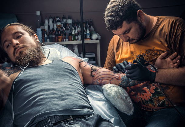 Especialista en tatuajes en el trabajo en la sala de tatuajes. / Tatuaje profesional haciendo tatuaje en el salón
. - Foto, Imagen