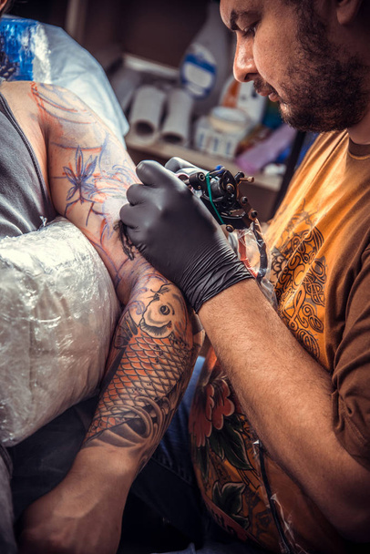 Ammattimainen tatuoija tekee tatuointia tatuointistudiossa
 - Valokuva, kuva