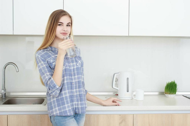 Beautiful young woman holds a glass with water on kitchen. - Фото, зображення