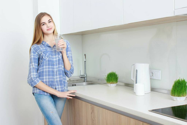 Beautiful young woman holds a glass with water on kitchen. - Φωτογραφία, εικόνα