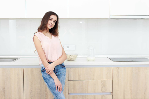 Serious attitude. Young smiling lady standing in a kitchen. - Foto, Bild
