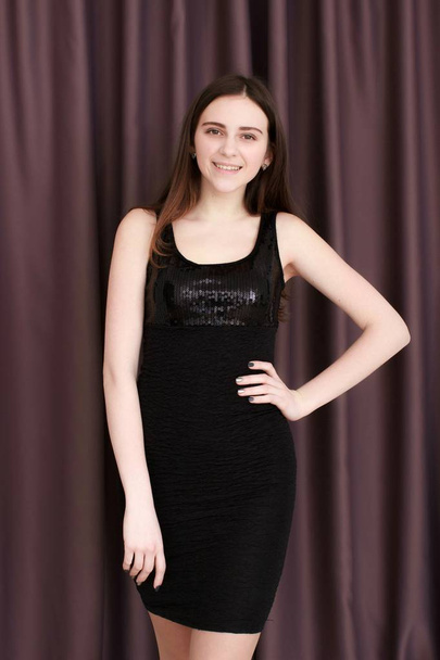 Young girl with black dress against curtains. Looking at the camera - Foto, Imagen