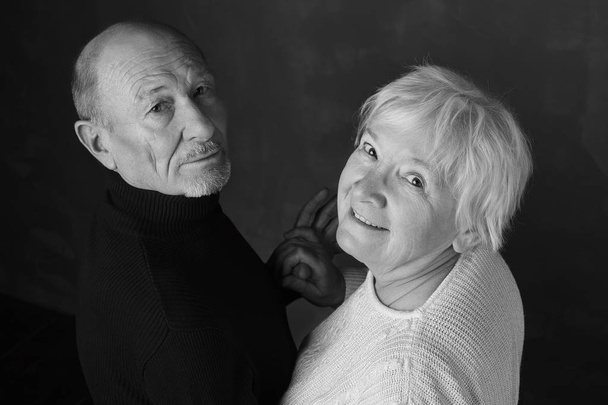 Ritratto d'amore infinito. Ritratto in bianco e nero di felice coppia anziana che si guarda e sorride in piedi in casa mano a mano su uno sfondo scuro
 - Foto, immagini