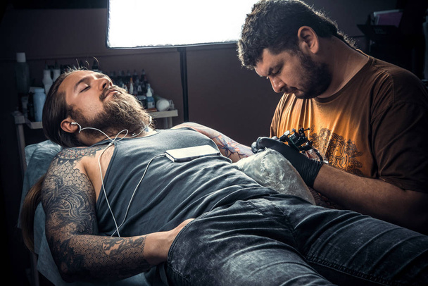 Мастер татуировки показывает процесс создания татуировки в тату-салоне
 - Фото, изображение