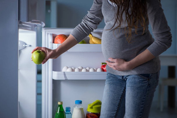 Pregnant woman near fridge looking for food and snacks at night - Фото, изображение