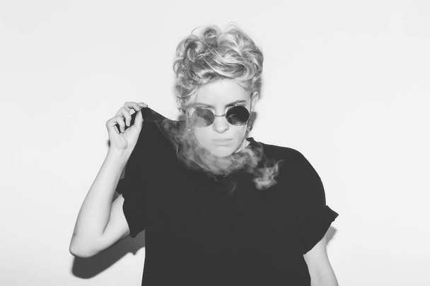 Stylish fashion sexy blonde bad girl in a black t-shirt and rock sunglasses. Dangerous rocky emotional woman. white toned. background, not isolated - Foto, imagen