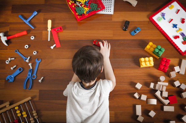 Top view of little boy lying on the wooden floor and playing with colorful toys. - Photo, Image