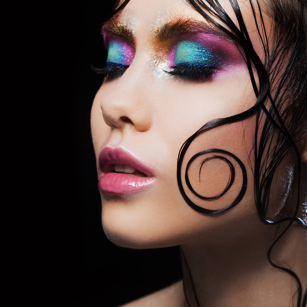 Young beautiful girl bright makeup with a wet look shine, dark background - Foto, afbeelding