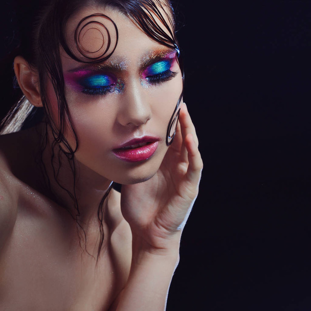 Young beautiful girl bright makeup with a wet look shine, dark background - Photo, Image