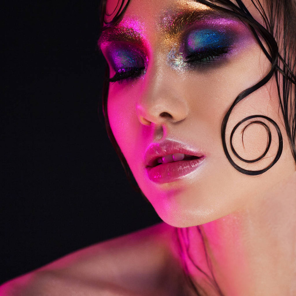 Young beautiful girl bright makeup with a wet look shine, dark background, pink light, disco style - Foto, Imagen