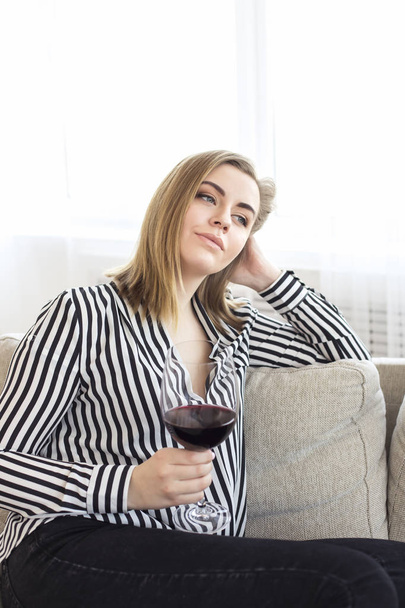 Attractive woman rests at home herself after a hard working day. In her hands holds a large glass of red wine - Fotó, kép