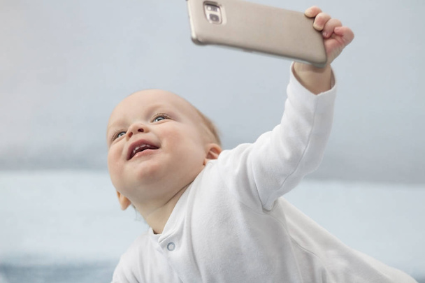 Cute infant boy makes selfie with a cell phone. Adorable smiling toddler kid taking a selfie photo with smartphone. - Photo, Image