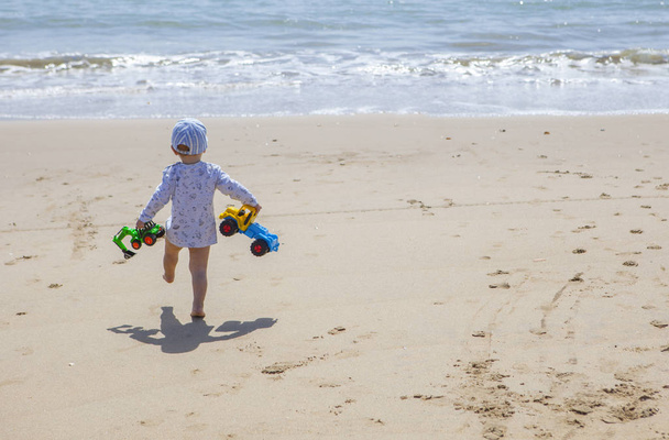Μωρό αγόρι να περπατά με παιχνίδια στην παραλία - Φωτογραφία, εικόνα
