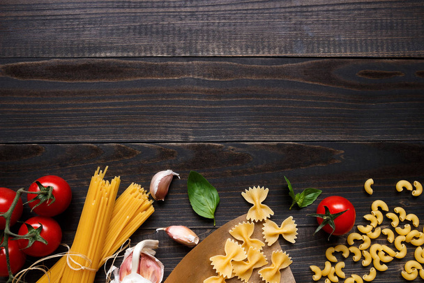 Dried mixed pasta and vegetables on the dark wooden table top view, with copy space - Фото, зображення