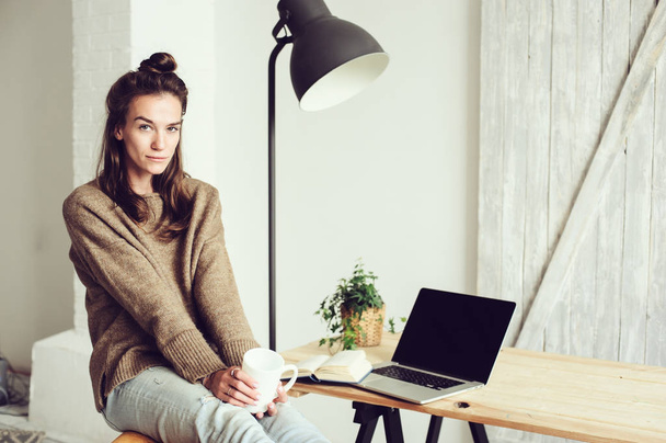 young beautiful blogger woman shopping at home online with laptop and cup of coffee in the morning. Home office in modern scandinavian interior - Fotografie, Obrázek