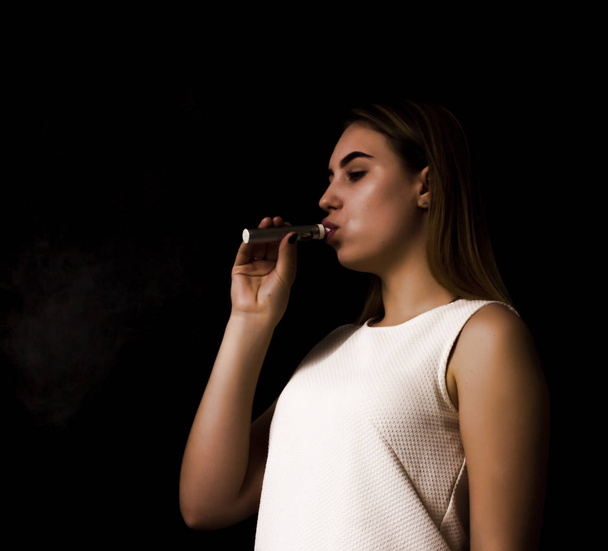 Pretty young girl uses electronic cigarette - Foto, afbeelding