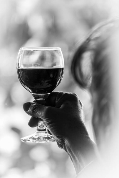 Kobieta trzyma wysoki, kieliszek czerwonego wina i oglądanie go - czarno-biały obraz - Zdjęcie, obraz