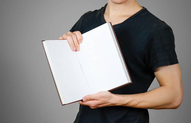 Closeup of guy in black t-shirt holding blank open white book on - Foto, afbeelding