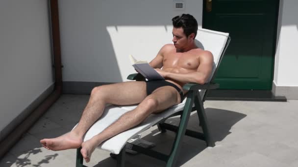 Young Man Sunbathing on Lounge Chair Reading Book - Imágenes, Vídeo