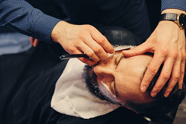 Barber shaving a man with a sharp razor - Foto, afbeelding