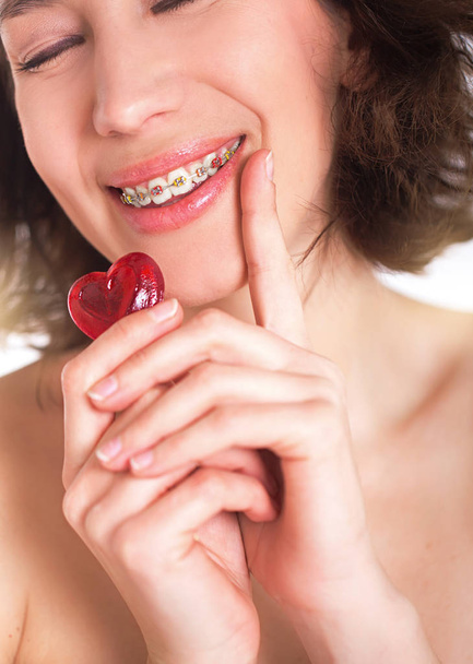 Beautiful girl with perfect skin and multi-colored braces posing with small heart in hands - Foto, Imagen
