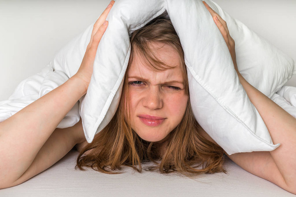 Frau im Bett deckt Ohren wegen Lärm mit Kissen ab - Foto, Bild