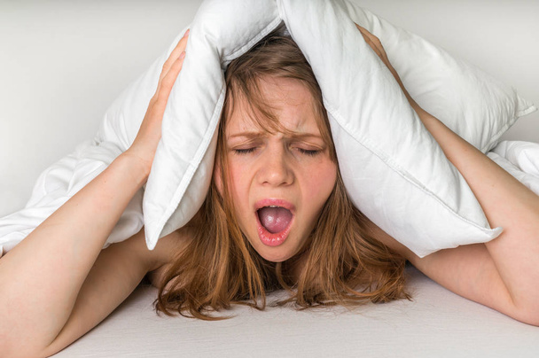Nainen unettomuus kattaa pään ja korvat tyynyllä
 - Valokuva, kuva