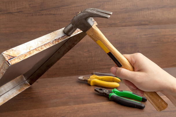 Mann greift Hammer zum Schlagen oder Fixieren von rostfreiem Tablett auf Holzboden - Foto, Bild