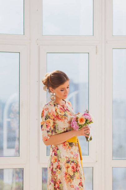 Beautiful girl in a long dress standing near a window with a bouquet - Foto, Imagem