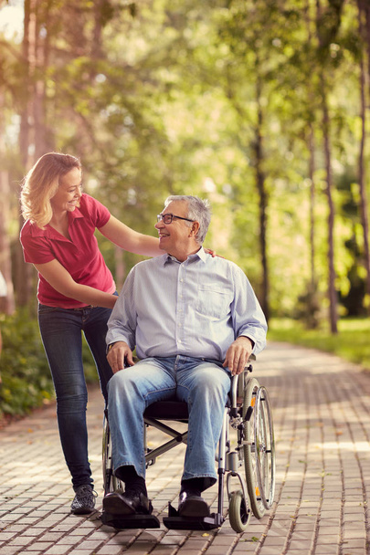 Mujer joven sonriente con su padre discapacitado en silla de ruedas
 - Foto, Imagen