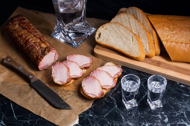 Flasche und Schnapsglas mit Wodka mit geräucherten Fleischscheiben auf dem Tisch - Foto, Bild