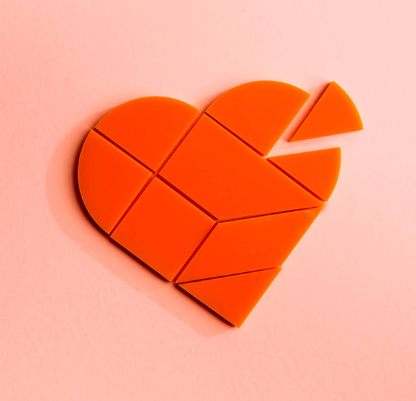 Plastic puzzle in the form of heart with disconnected piece on a pink background - Photo, Image