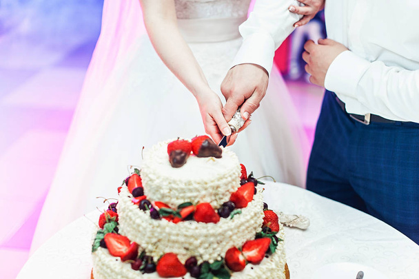 свадебная церемония. невеста и жених делают свой первый кейс вместе, вырезают свадебный торт
 - Фото, изображение