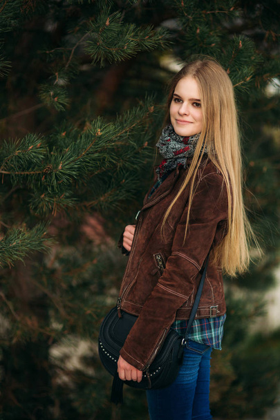 A beautiful girl is walking along the embankment. Blond hair and brown jacket. Spring. - Photo, Image