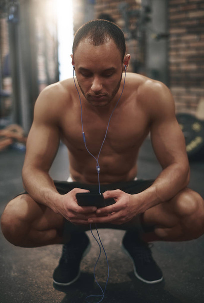 hombre escuchando música mientras está sentado en el gimnasio
 - Foto, Imagen