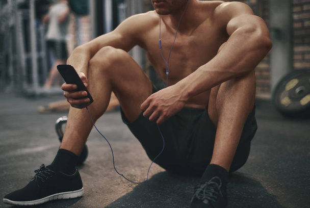 hombre escuchando música mientras está sentado en el gimnasio
 - Foto, Imagen