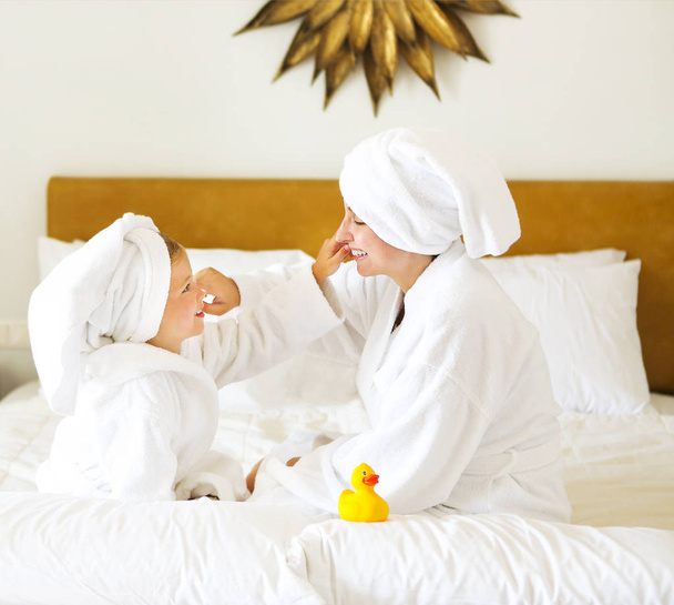 Happy mother and daughter in bathrobes with cream mask - Φωτογραφία, εικόνα