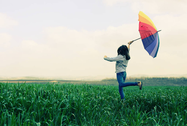 Mädchen mit Regenschirm springt in Feld  - Foto, Bild